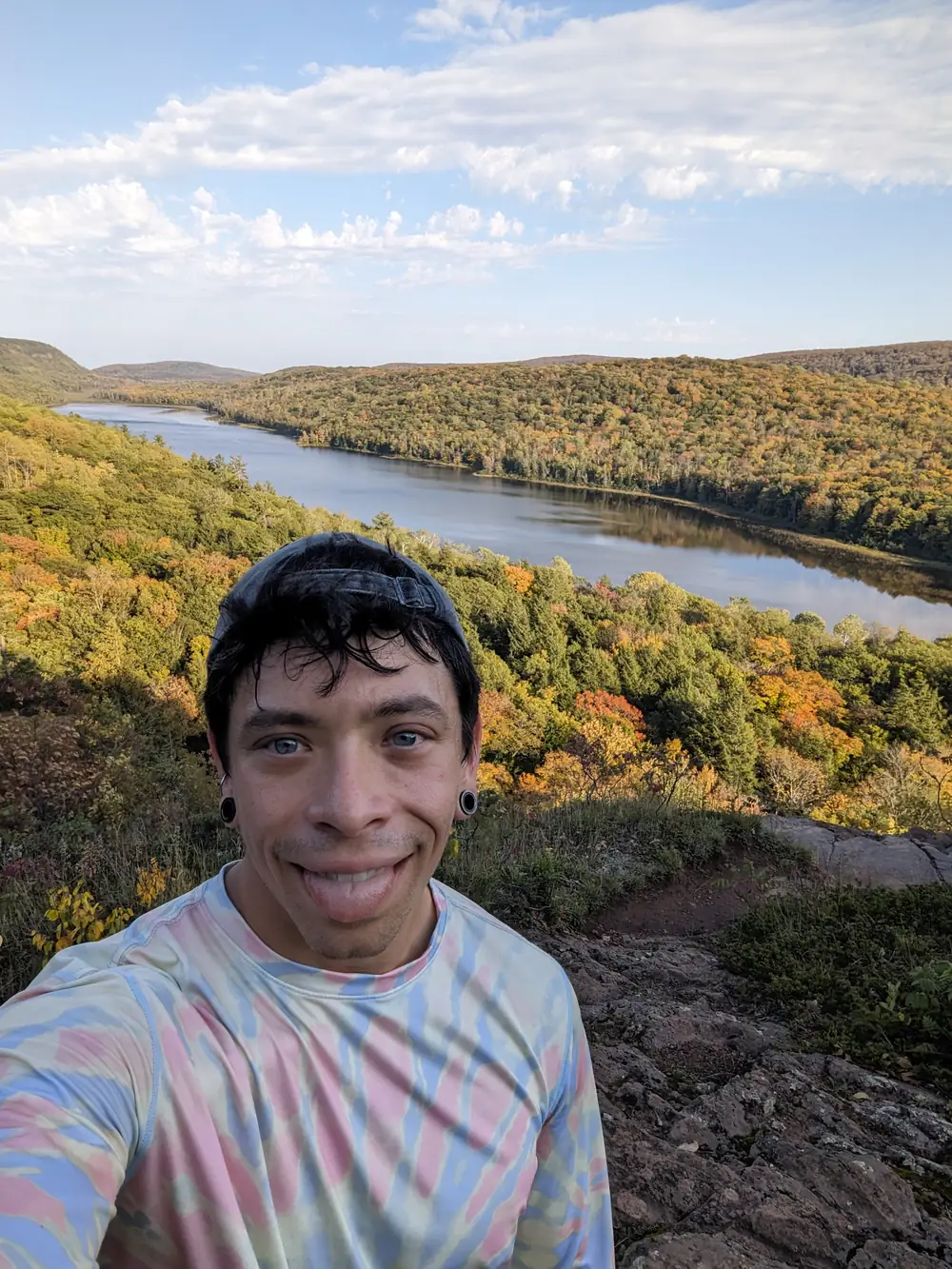 Jason Osaj at the Lake of the Clouds overlook in the Porcupine Mountains, autumn colour running along the ridge behind him