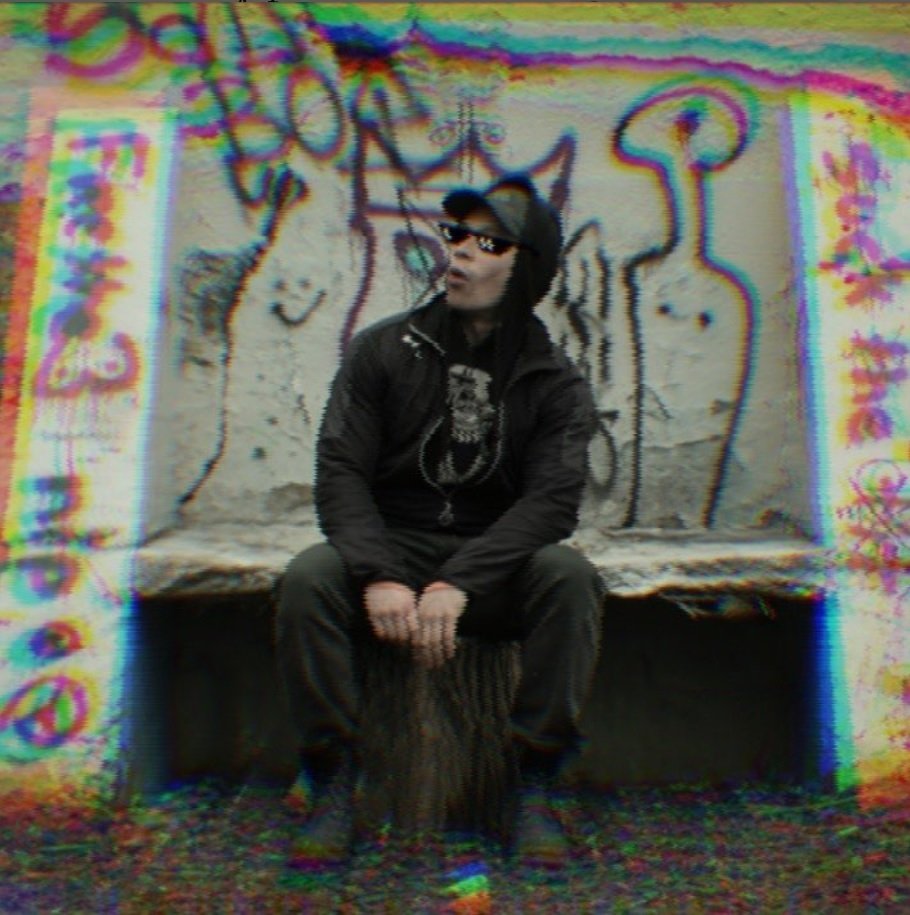 Jason Osaj in a black hooded jacket, seated against a graffiti wall, rendered with an RGB glitch shift